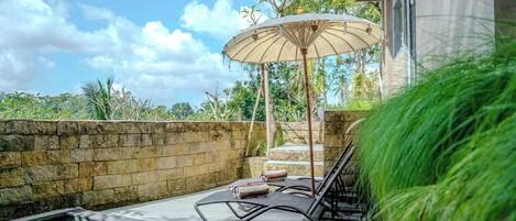 A pool area with lounge chairs, a stone wall, and an umbrella.