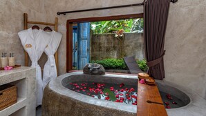A stone bathtub with rose petals, a wooden bench, and a window with a view of greenery. - Hoshi Jungle Resort by Dhananjaya Hospitality (Tegallalang)