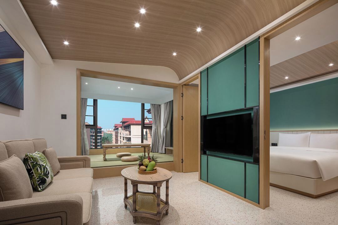 A modern hotel room with a sofa, a round table with fruits, a TV, and a bed.