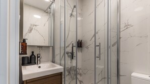 Un baño moderno con cabina de ducha de mármol, un lavabo con mueble de madera y un inodoro.
