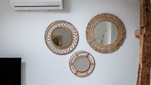 Un comedor con una mesa y sillas de madera, un televisor y tres espejos tejidos en la pared.