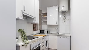 Une cuisine compacte avec des meubles blancs, un four encastré, un four à micro-ondes, un lave-vaisselle et un chauffe-eau.