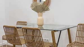 Un coin repas comprenant une table ronde en verre, six chaises en osier et trois miroirs fixés au mur.