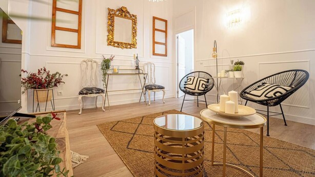 A modern living room with a fireplace, two ornate mirrors, a round coffee table, and two black wire chairs.