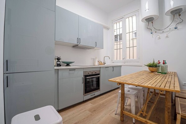 Una cocina compacta con armarios grises, una mesa de madera y una ventana con marcos blancos.