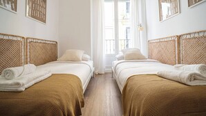 A hotel room with two beds, each with a woven headboard, white linens, and a rolled towel.