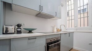 A modern kitchen with white cabinets, a built-in oven, a toaster, and a window with blinds.