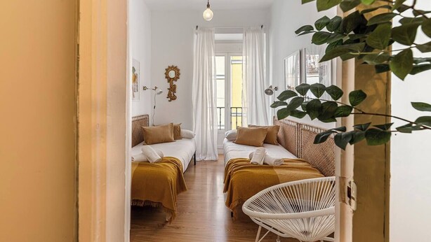 A hotel room with two beds, a white chair, a hanging plant, and a view of the street. - Malasaña Gold (Madrid)