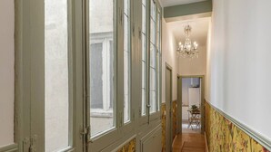 A hallway with a wooden floor, a chandelier, and a door leading to a room with a floral wallpaper. - Malasaña Gold (Madrid)