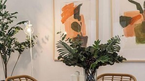 A dining area with a glass table, wicker chairs, and framed abstract art on the wall. - Malasaña Gold (Madrid)