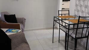 Una sala de estar con un sofá, una mesa de centro, una mesa de comedor con sillas y un televisor montado en la pared.