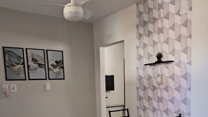 Una sala de estar moderna con comedor, paredes blancas, ventilador de techo, arte abstracto en la pared, una pequeña planta en maceta y un termostato.