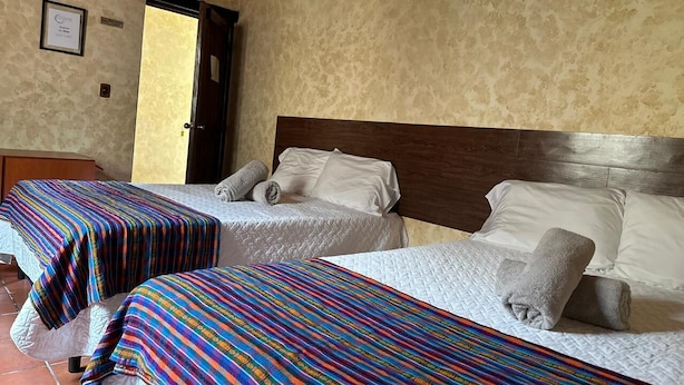 Two single beds with colorful striped bedspreads, a wooden headboard, and a door leading outside. - Casa Los Héroes (Antigua Guatemala)