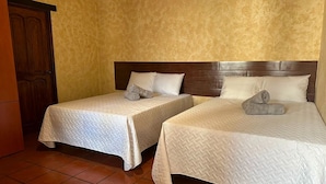 Two beds with white quilts and wooden headboards in a room with yellow textured walls and tiled flooring. - Casa Los Héroes (Antigua Guatemala)