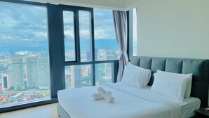 Une chambre d’hôtel avec un grand lit, une tête de lit grise et une vue sur le paysage urbain par une grande fenêtre.