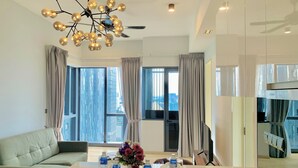 Une chambre d’hôtel moderne dotée d’une grande fenêtre, d’un canapé, d’une table à manger avec des bouteilles d’eau et un vase de fleurs, ainsi que d’un luminaire au plafond.