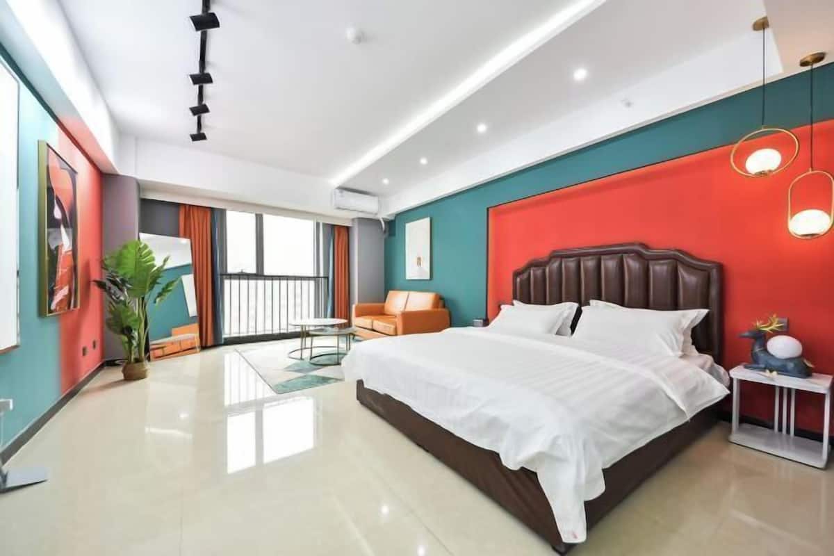 A modern hotel room with a large bed, a seating area with a sofa and a table, and a balcony with a view.