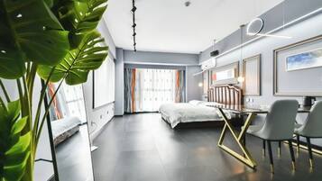 A modern hotel room with a bed, a desk with chairs, a large window with curtains, and a plant.