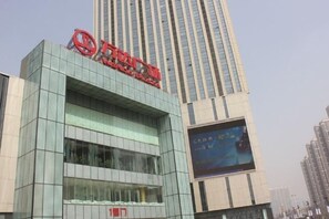 A modern building with a prominent red logo on the facade, large windows, and a billboard on the side. - Jinmei Hotel (Yuhua Wanda) (Shijiazhuang)
