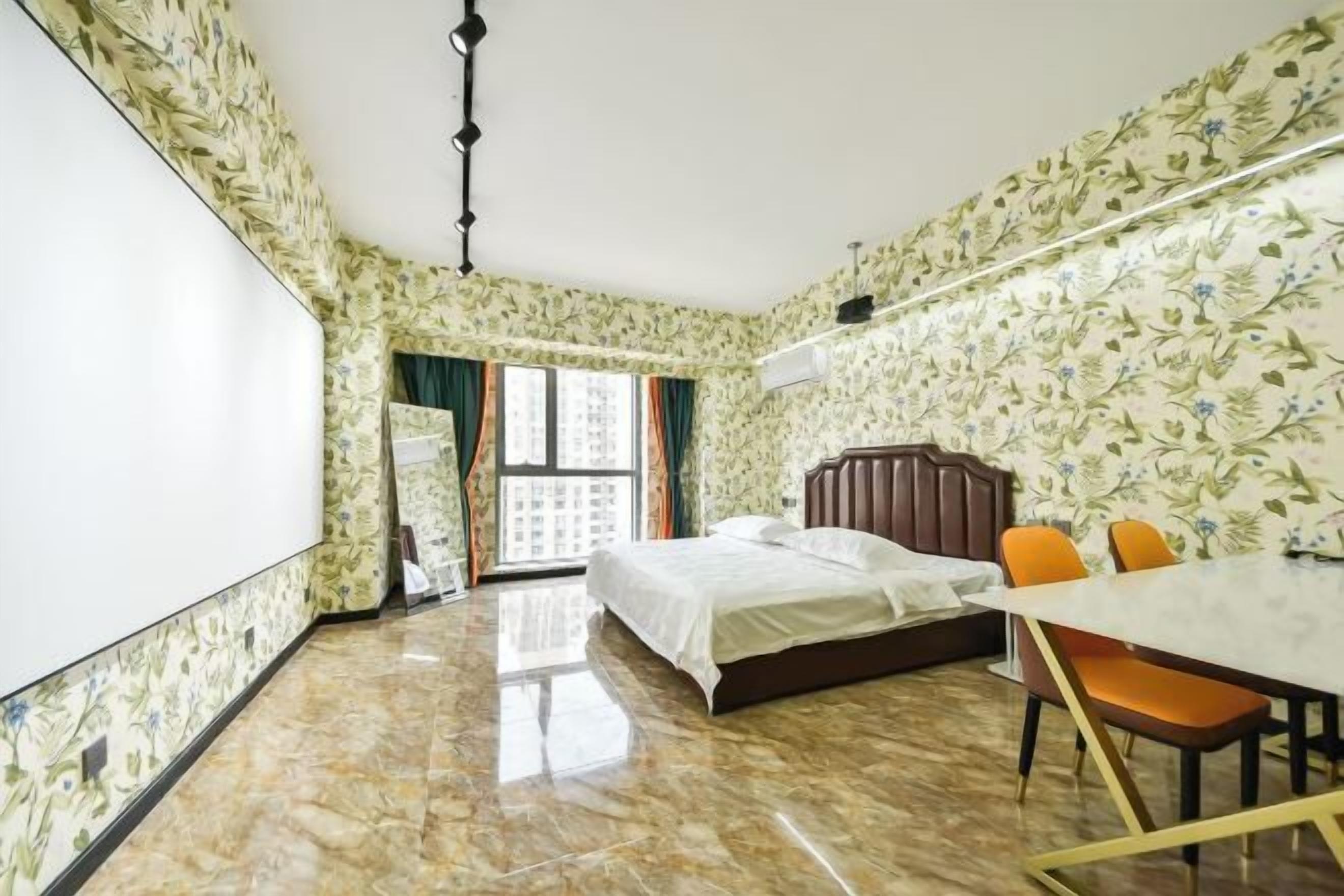 A hotel room with a bed, a dining table with chairs, a large window, and a view of buildings outside.