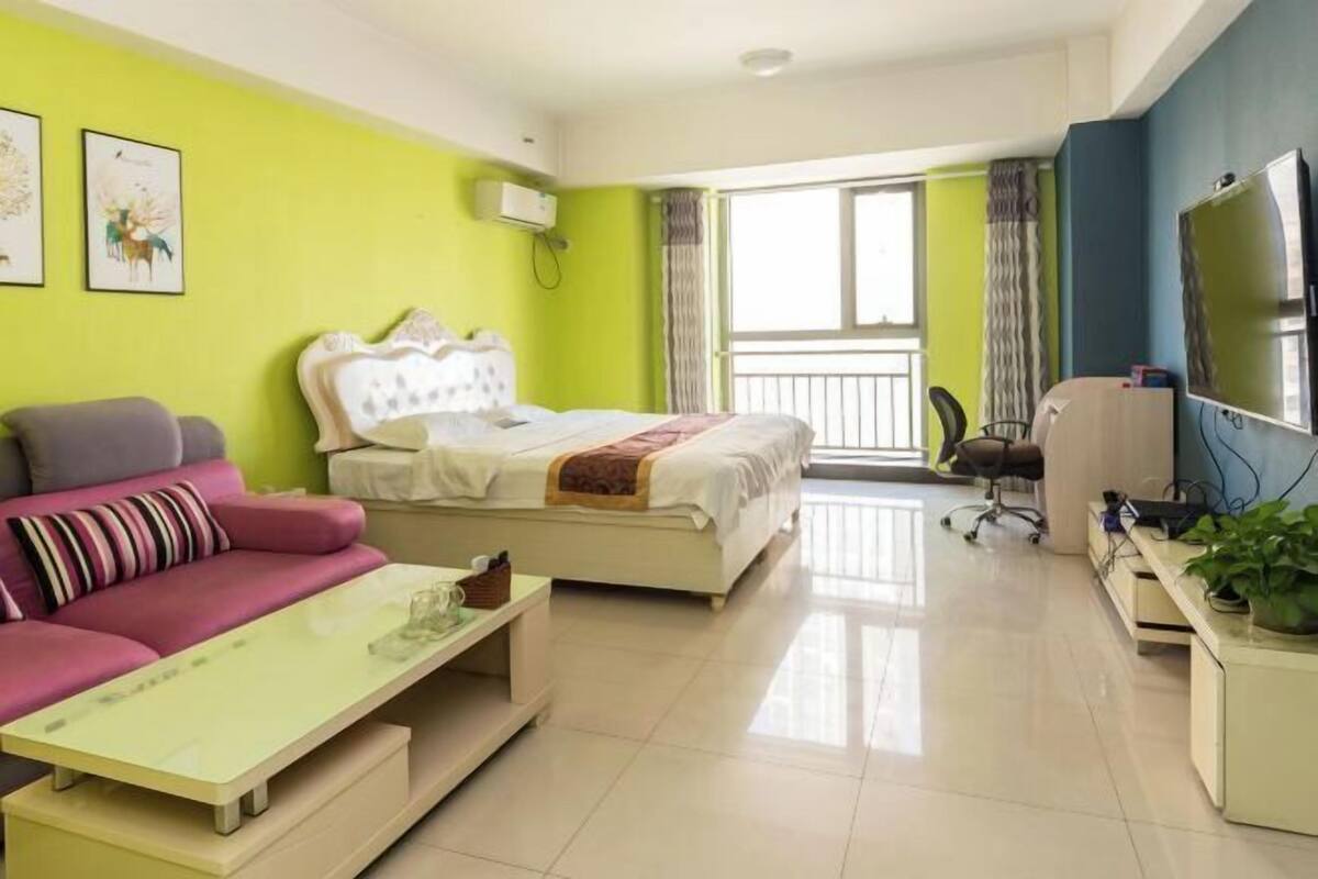 A modern hotel room with a bed, sofa, and a desk with a television.