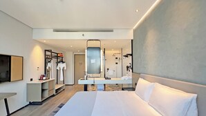 Ein modernes Hotelzimmer mit einem großen Bett, einem Flachbildfernseher, einem Schminktisch mit Spiegel und einer bodenebenen Dusche.