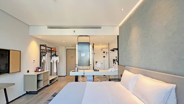 Een moderne hotelkamer met een groot bed, een flatscreen televisie, een kaptafel met spiegel en een inloopdouche.