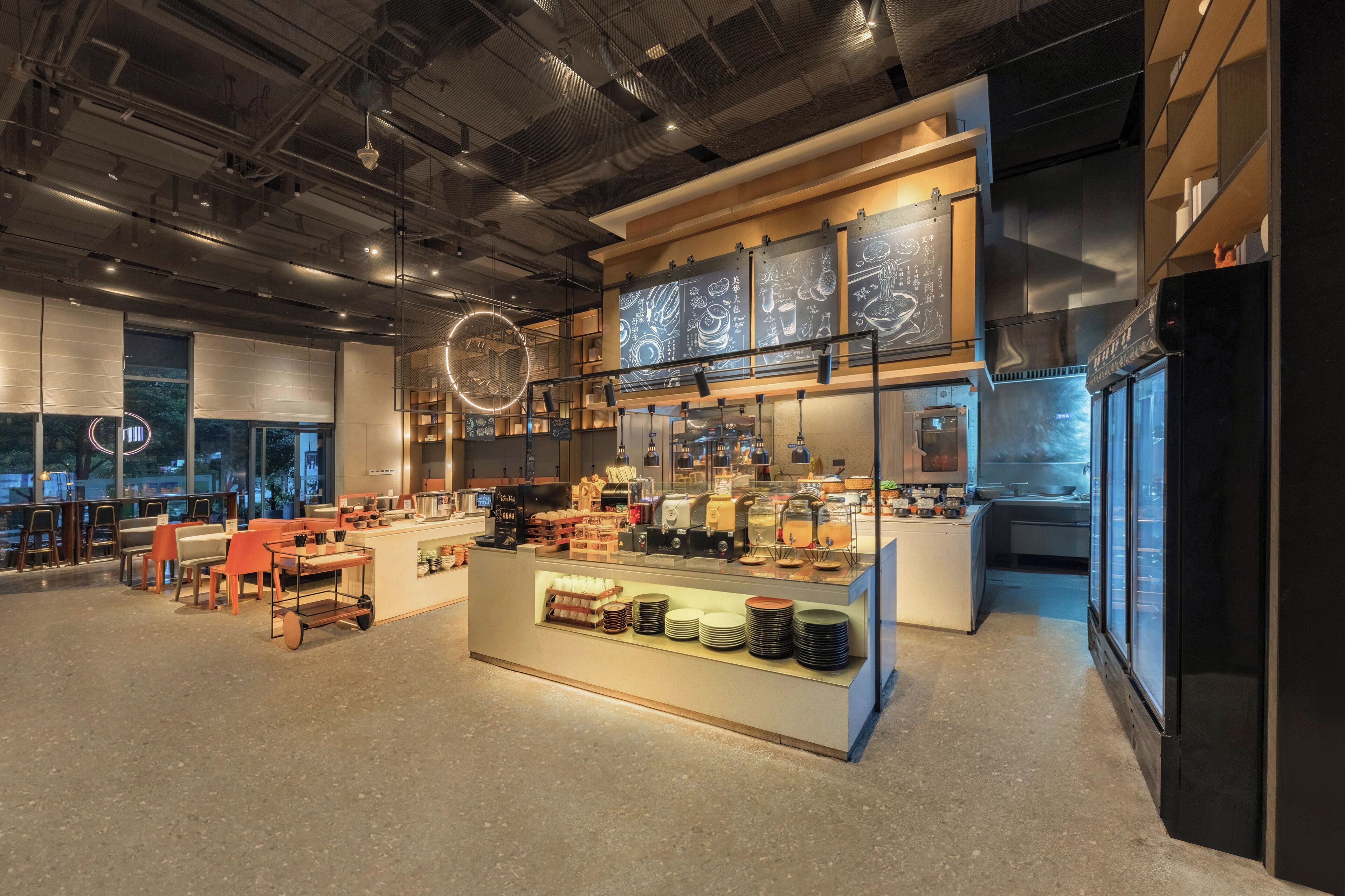 A modern cafe with a central counter, seating area, and a kitchen in the background.