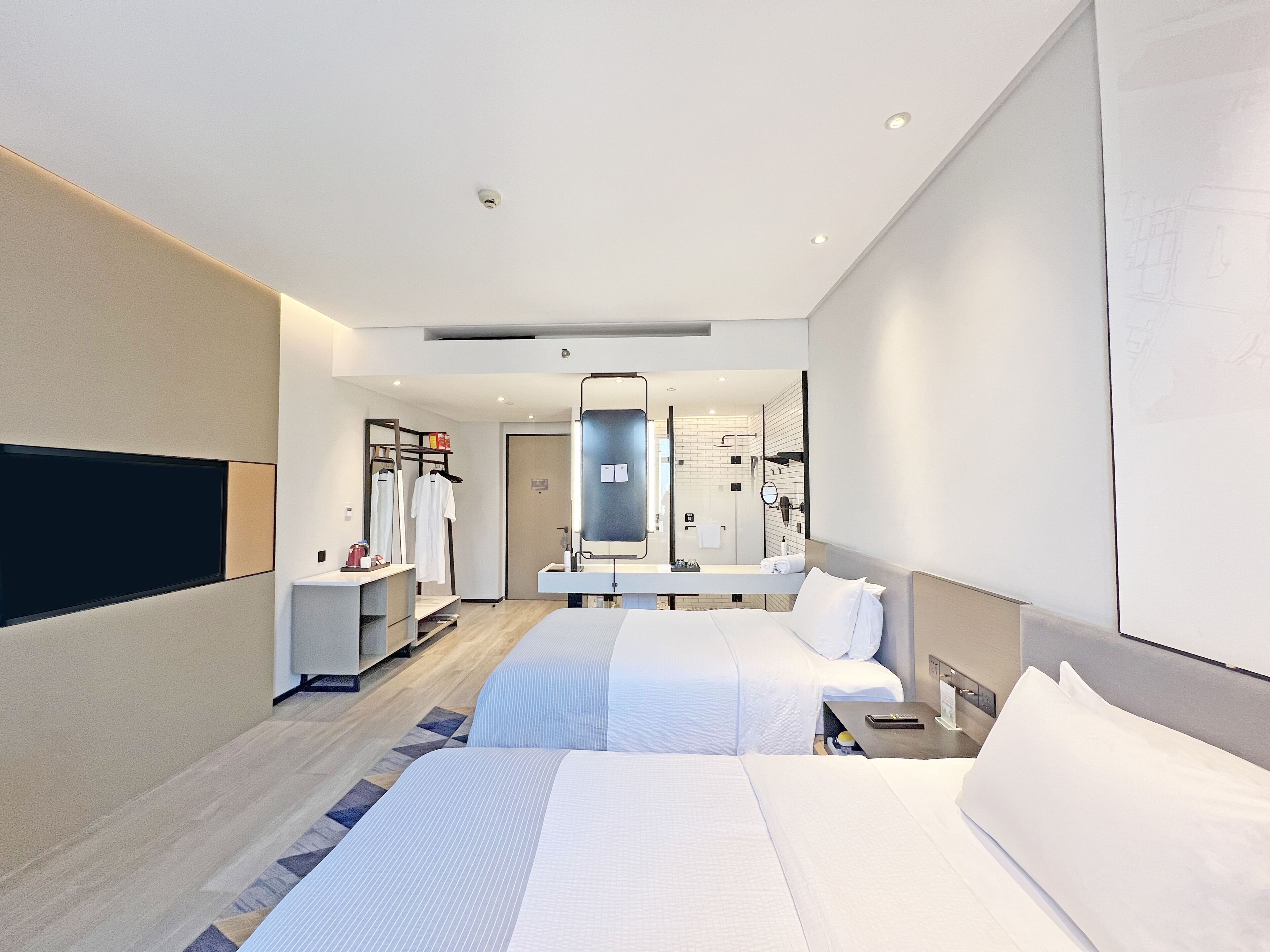 Una habitación de hotel moderna con dos camas, un espejo grande, un vestidor y un baño con cabina de ducha de vidrio.