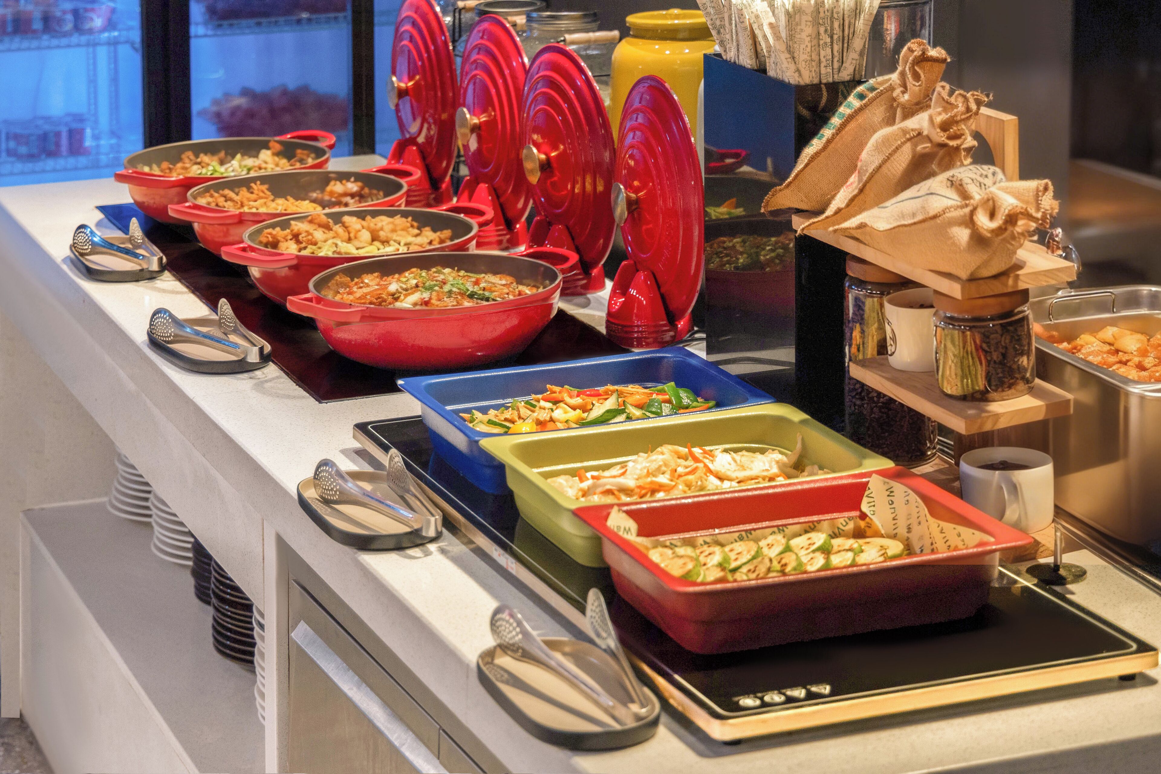 A buffet with various dishes in red and blue containers, a coffee station, and a window with a view.