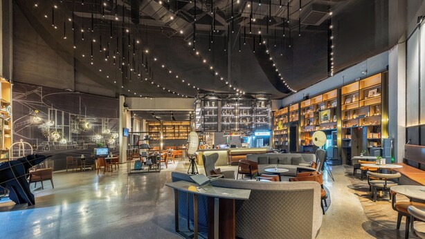 A spacious, modern interior with a central seating area, high ceilings with exposed ductwork, and a variety of seating options including sofas and tables. - Wanda Moments Neo Nanchang West Railway (Nanchang)