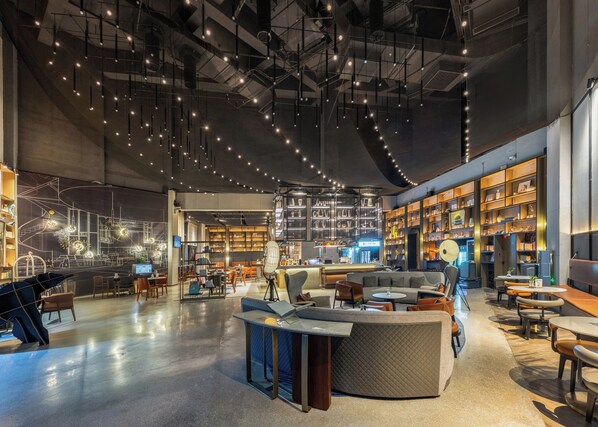A spacious, modern interior with a central seating area, high ceilings with exposed ductwork, and a variety of seating options including sofas and tables. - Wanda Moments Neo Nanchang West Railway (Nanchang)