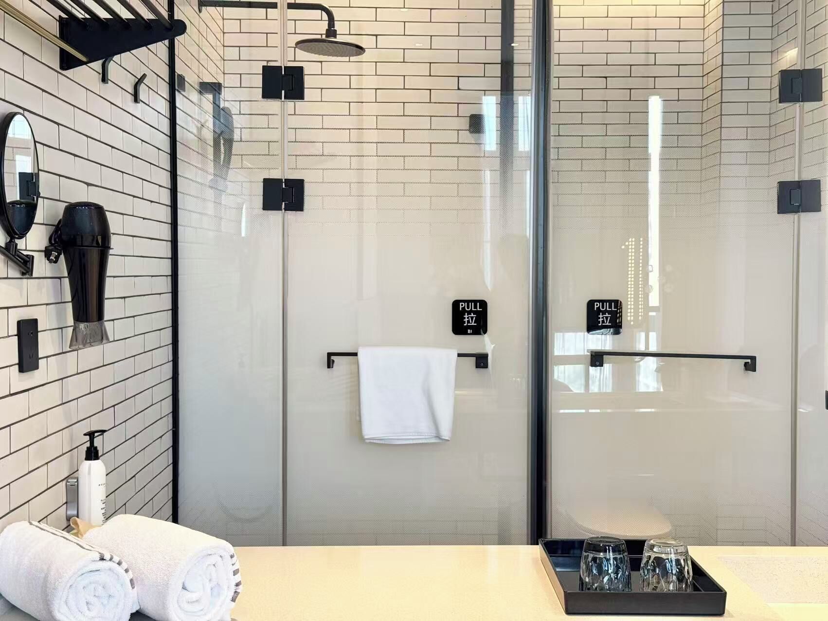 A modern bathroom with a glass shower enclosure, a towel rack, and a tray with glasses.