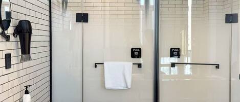 Un baño moderno con cabina de ducha de vidrio, un perchero y una bandeja con vasos.