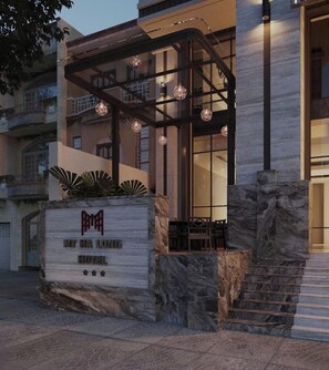 A hotel entrance with a stone facade, a staircase, and a covered outdoor seating area with hanging lights. - MT Collection Hotel Ha Long (Ha Long)