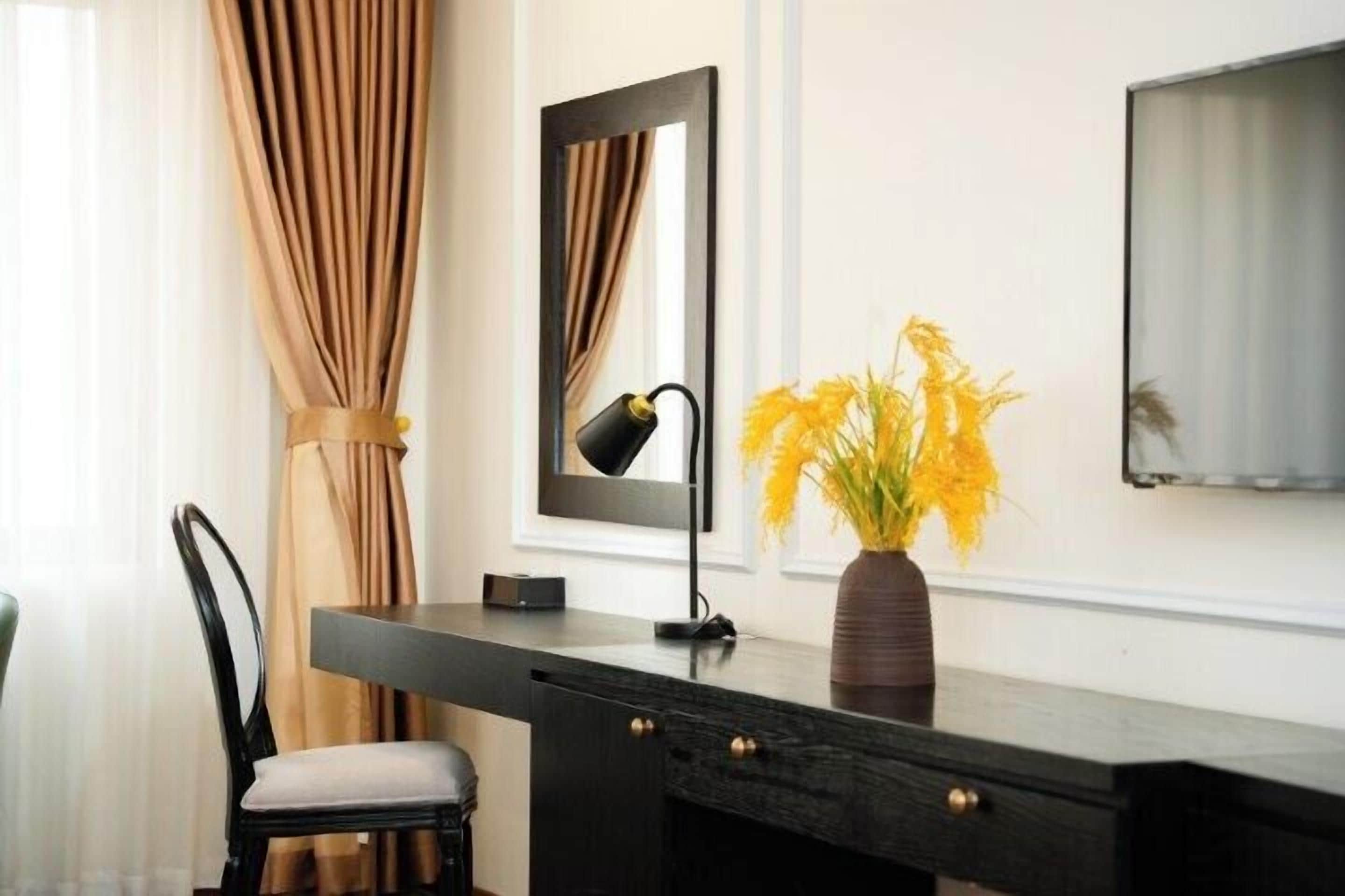 Un escritorio moderno con una silla, un espejo, un florero con flores amarillas y un televisor en la pared.