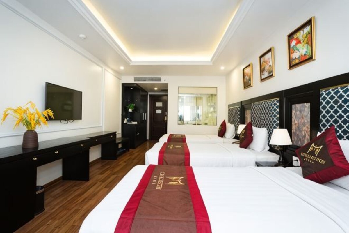 A hotel room with a long bed, a desk, a TV, and a view of the outside.