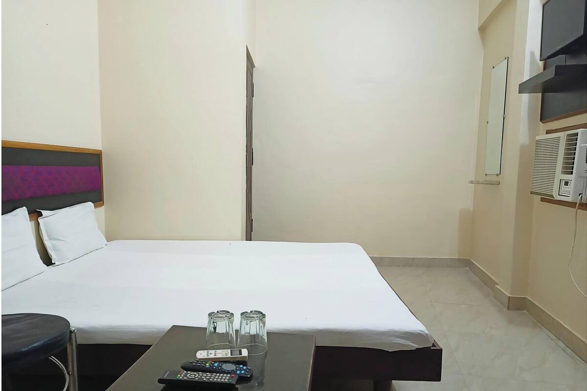 Ein Hotelzimmer mit einem Bett, einem kleinen Tisch mit Fernbedienung und einer Wandklimaanlage.
