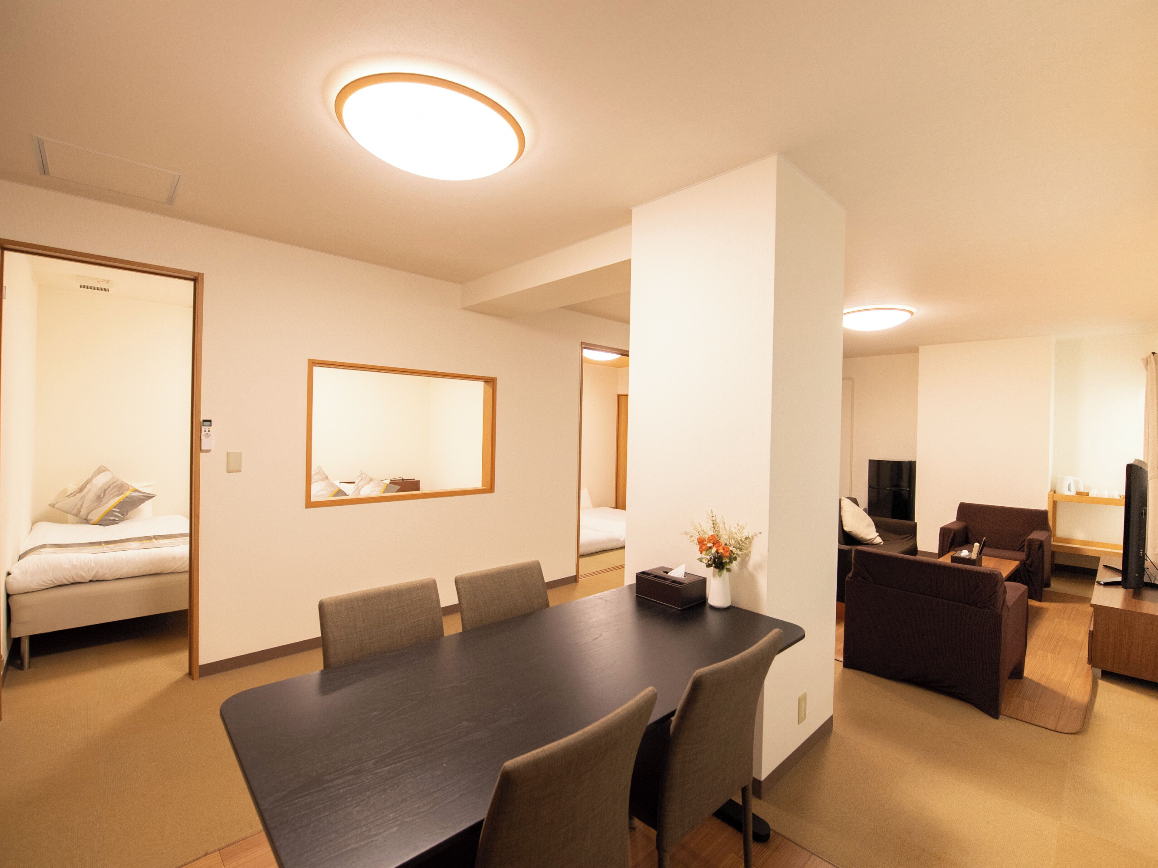 A hotel room with a dining table, chairs, a sofa, a TV, and a bed.