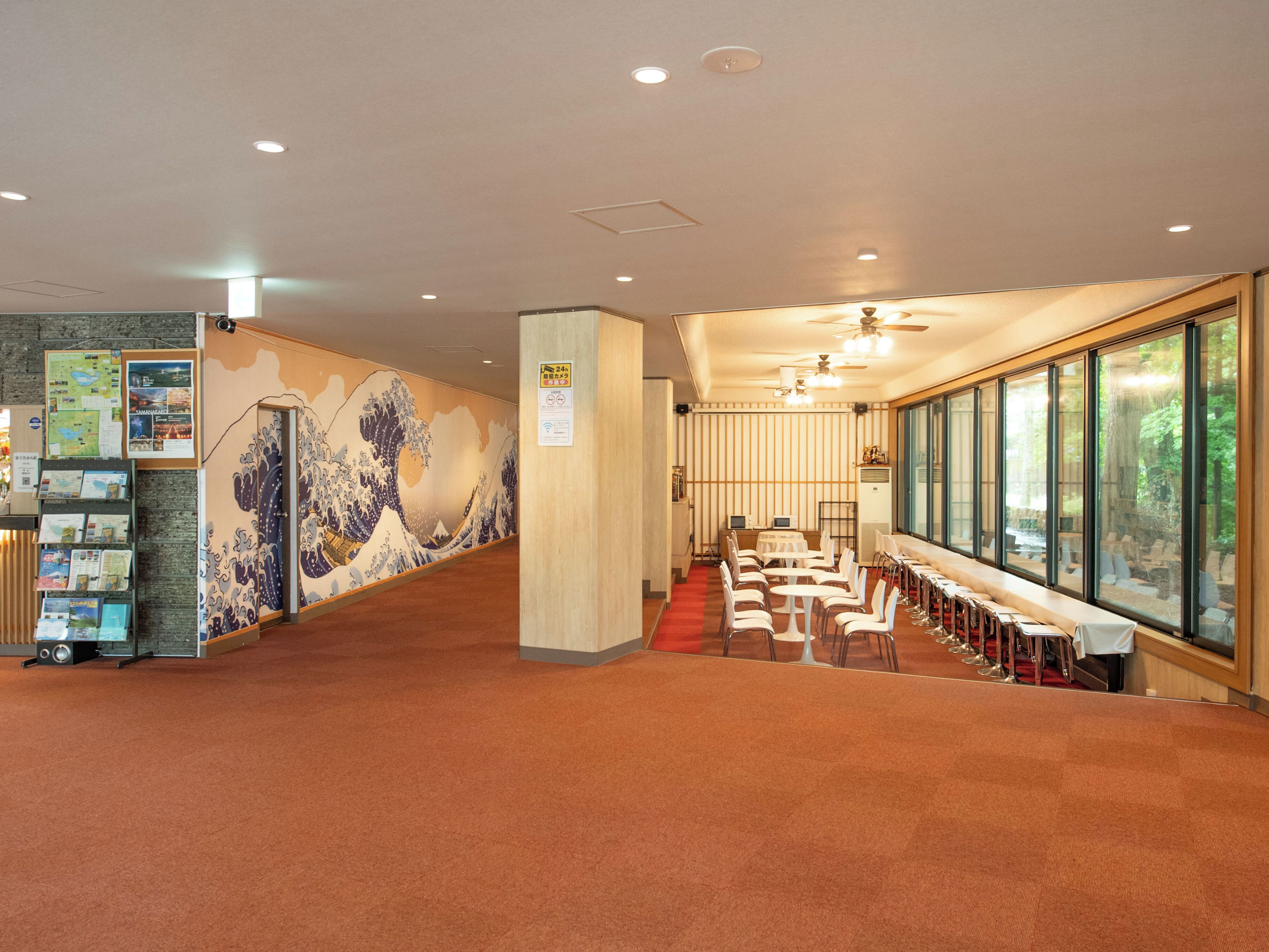 Eine Hotelhalle mit traditioneller japanischer Wandmalerei, einem Empfangsschalter mit Broschüren und einer Sitzecke mit Tischen und Stühlen.