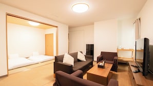 Habitación de hotel moderna con sofá, una mesita, televisor y suelo de madera.