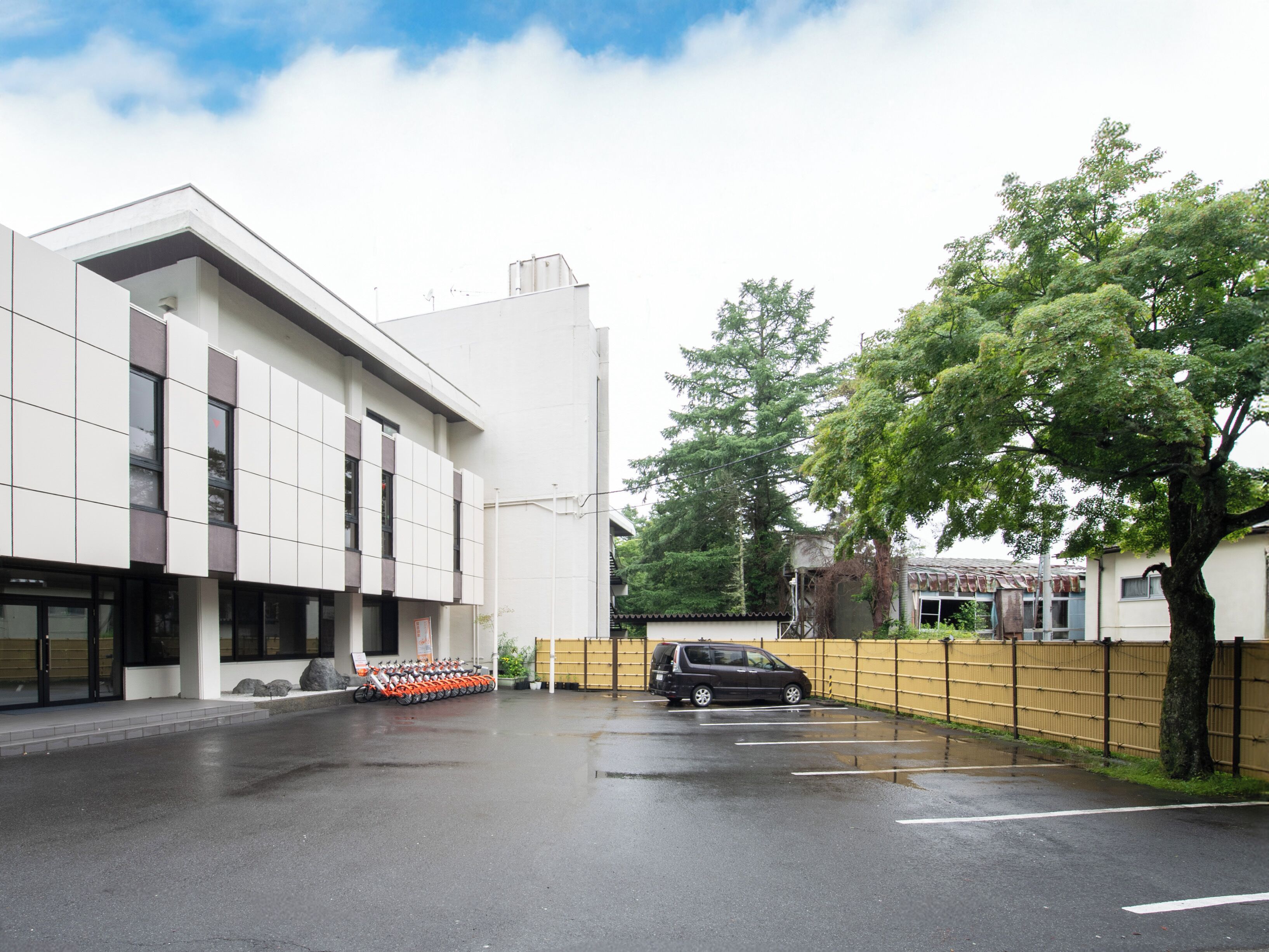 Un edificio moderno con un parcheggio, una zona coperta e una strada alberata.