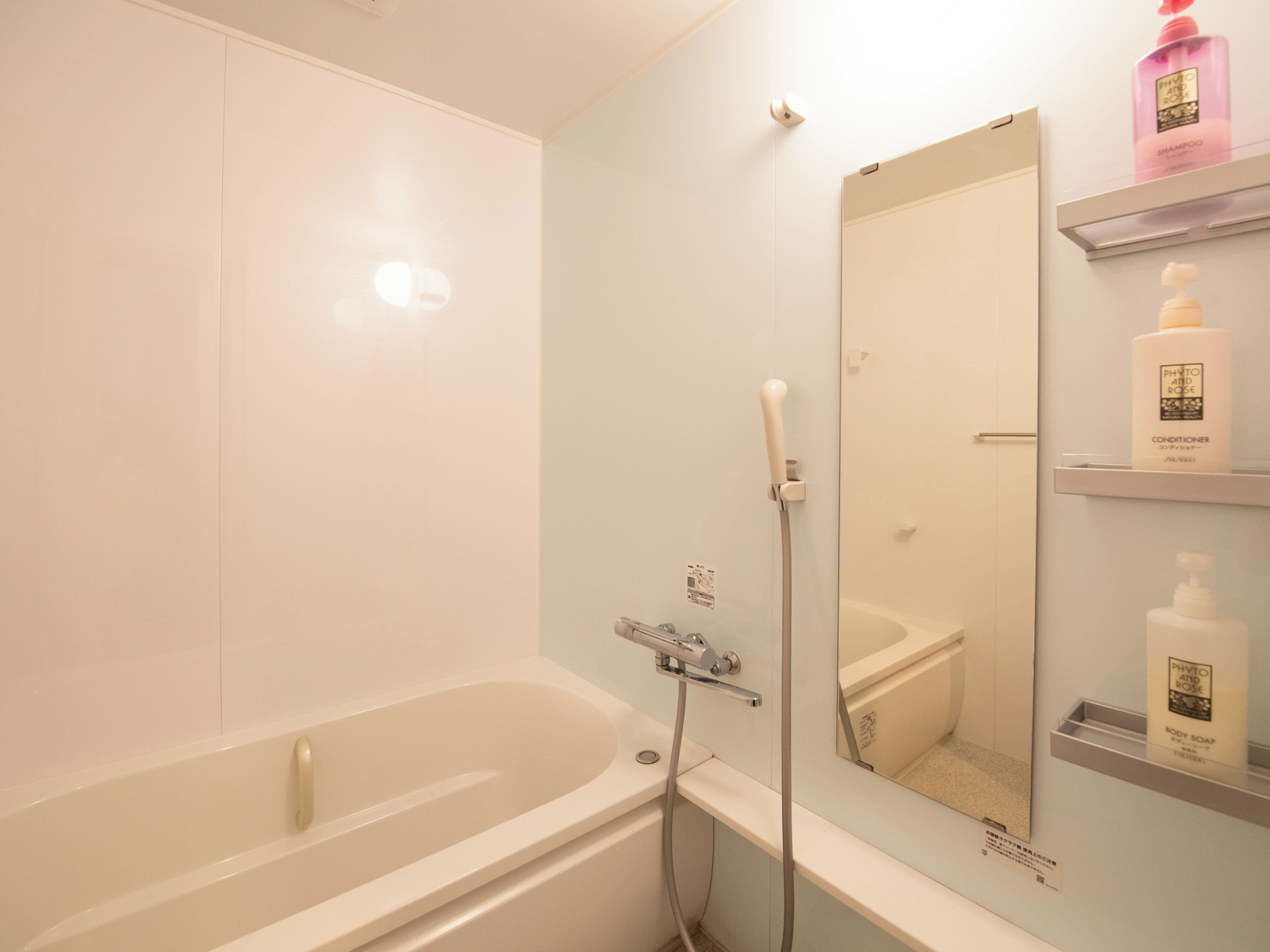 A bathroom with a bathtub, a shower, a mirror, and shelves with toiletries.