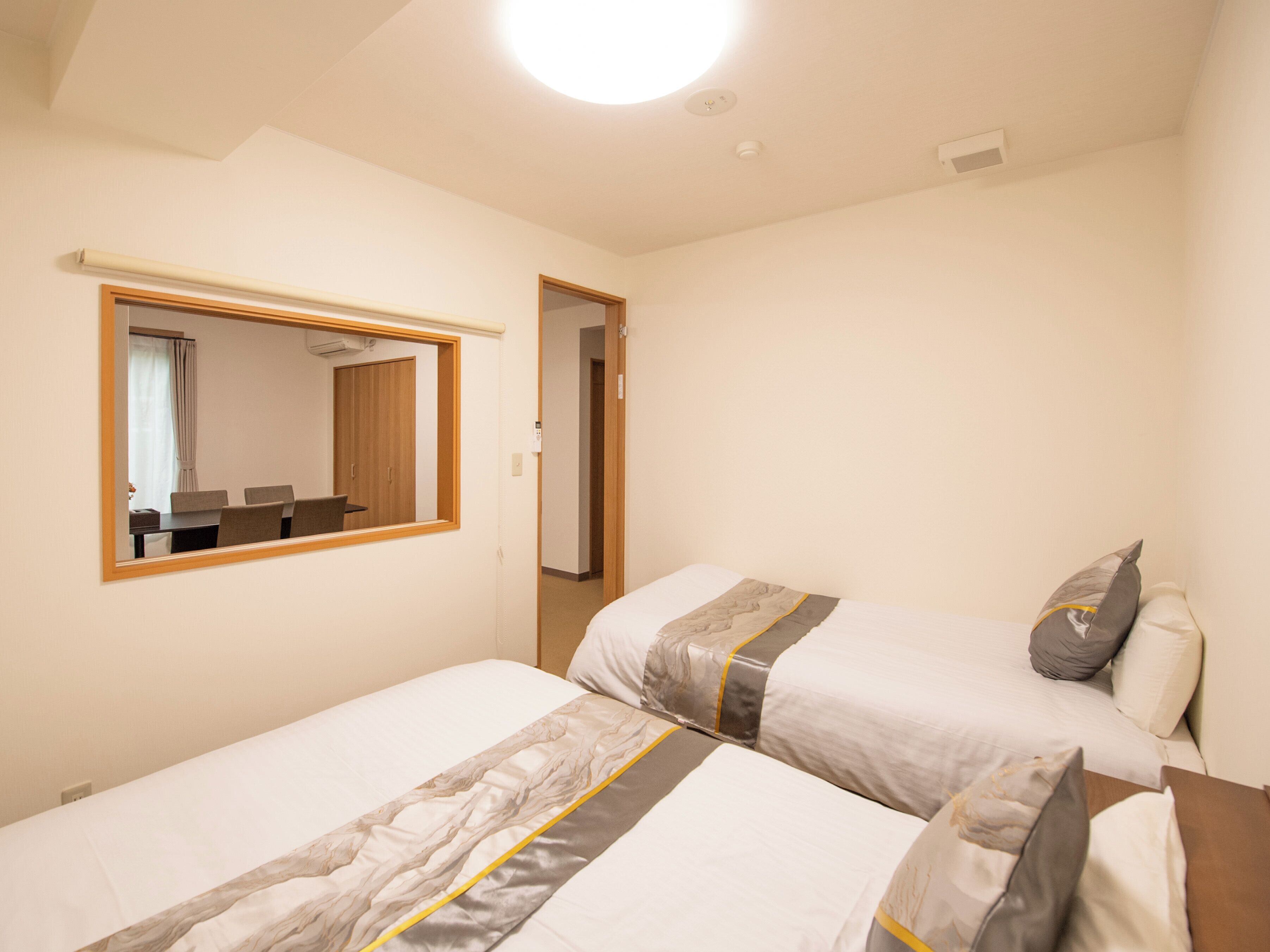 A hotel room with two beds, a mirror, a desk, and a chair.