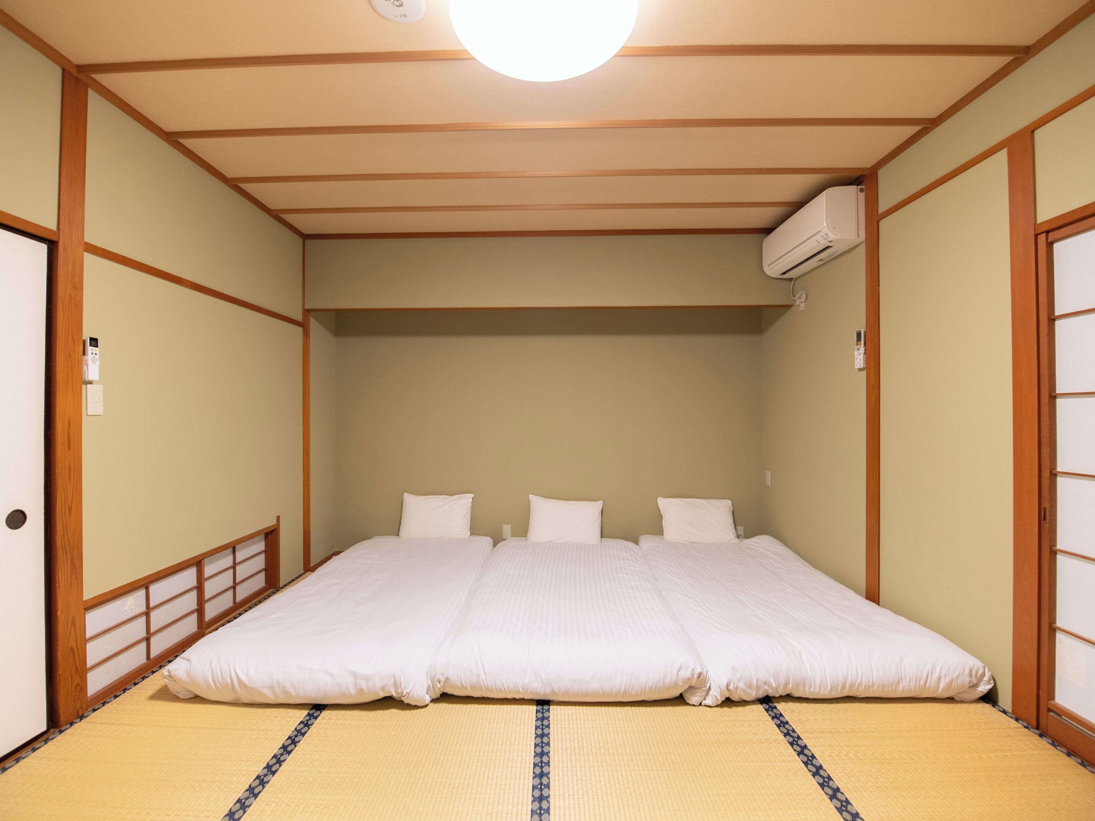 A traditional Japanese-style room with tatami flooring, a low ceiling, and a bed with white bedding.