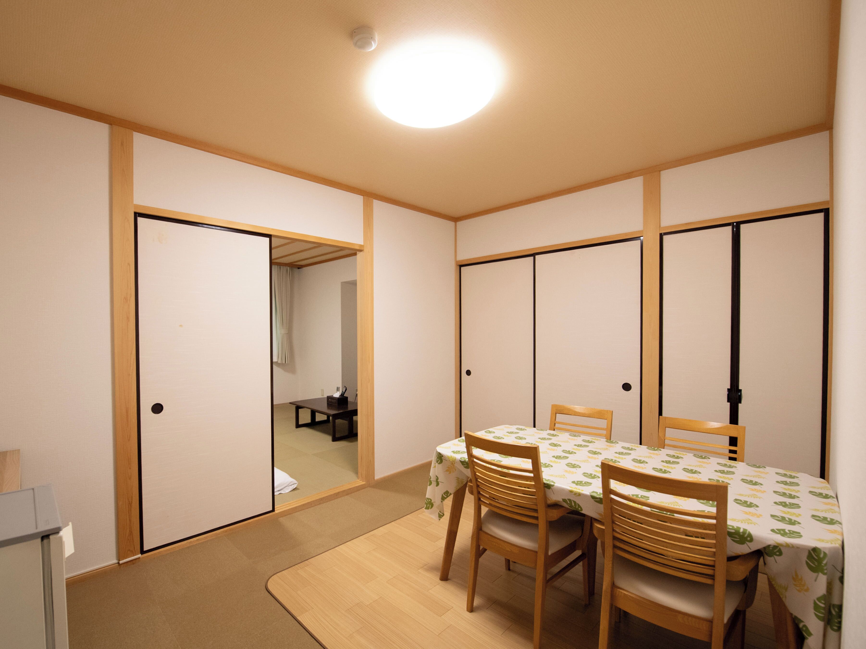 Una habitación tradicional japonesa con suelo de tatami, una mesa baja con sillas y puertas correderas.