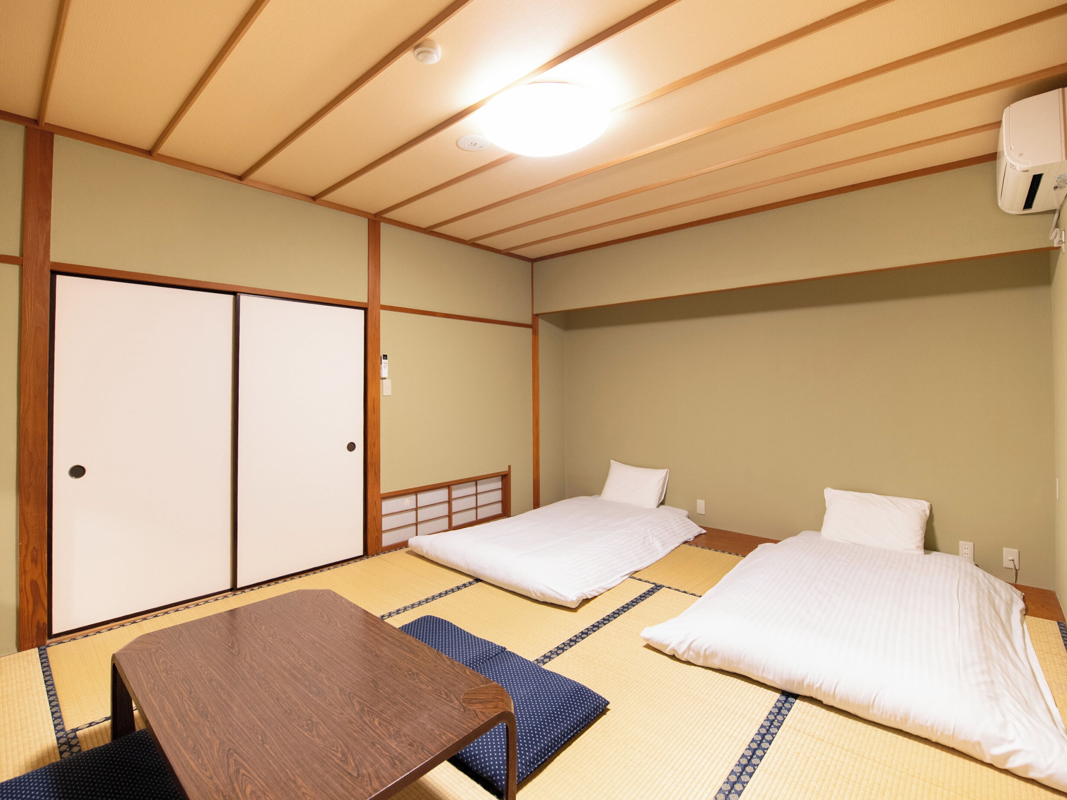 A traditional Japanese room with tatami flooring, two single beds, a wooden table, and a sliding door.
