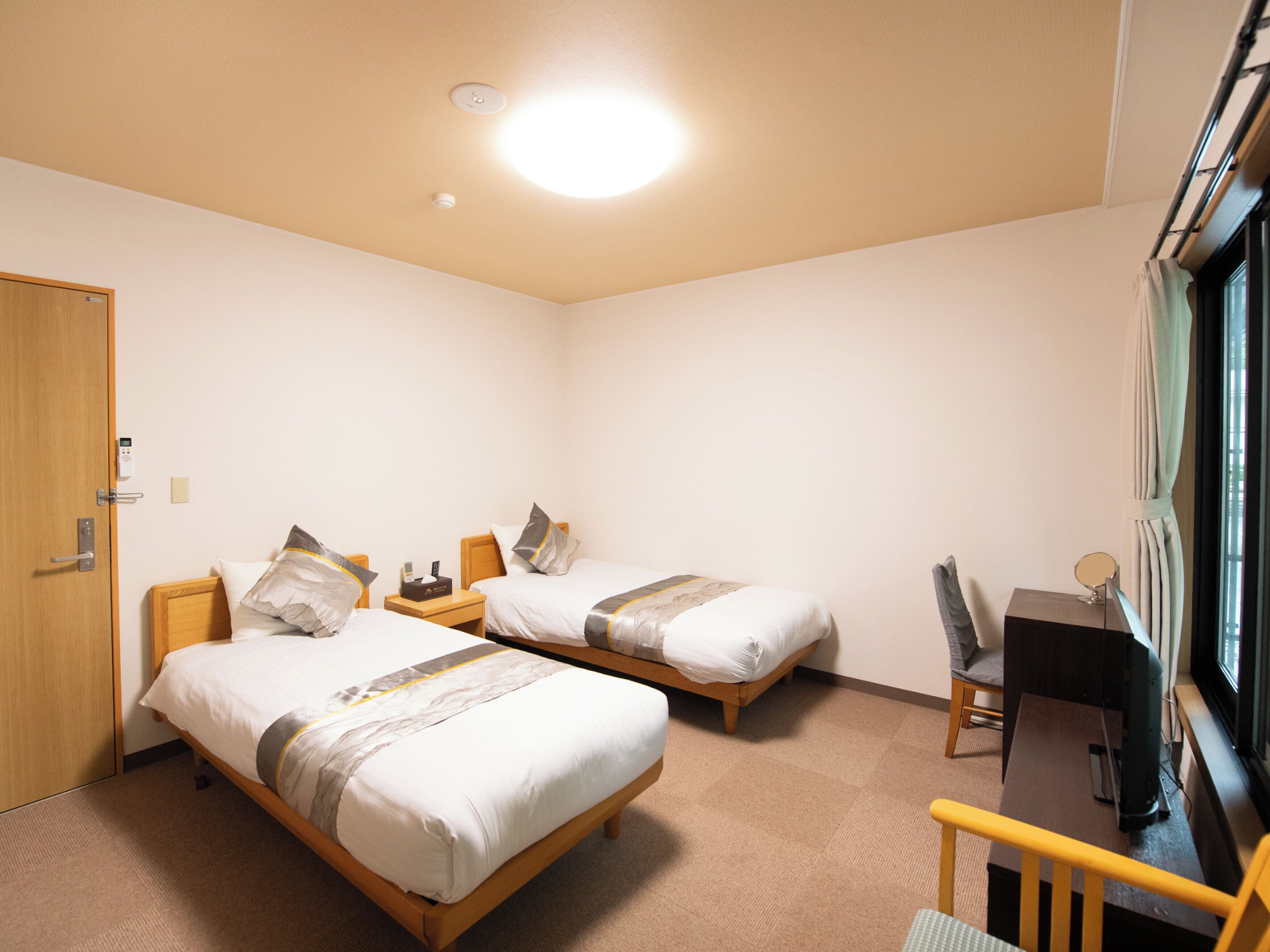 Een hotelkamer met twee bedden, een bureau, een stoel, een televisie en een raam.