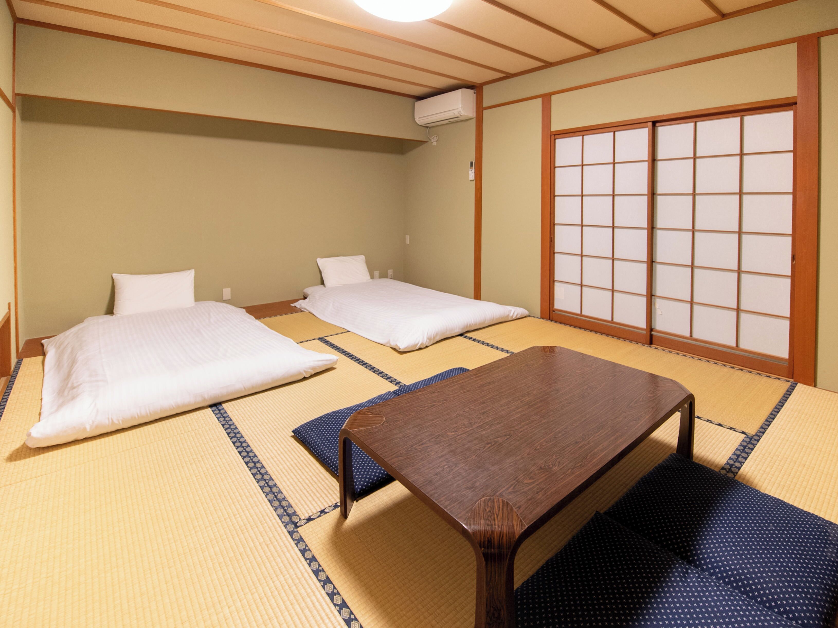 Une pièce de style japonais traditionnel, avec un sol recouvert de tatamis, deux lits, une table en bois et un paravent coulissant de type shoji.