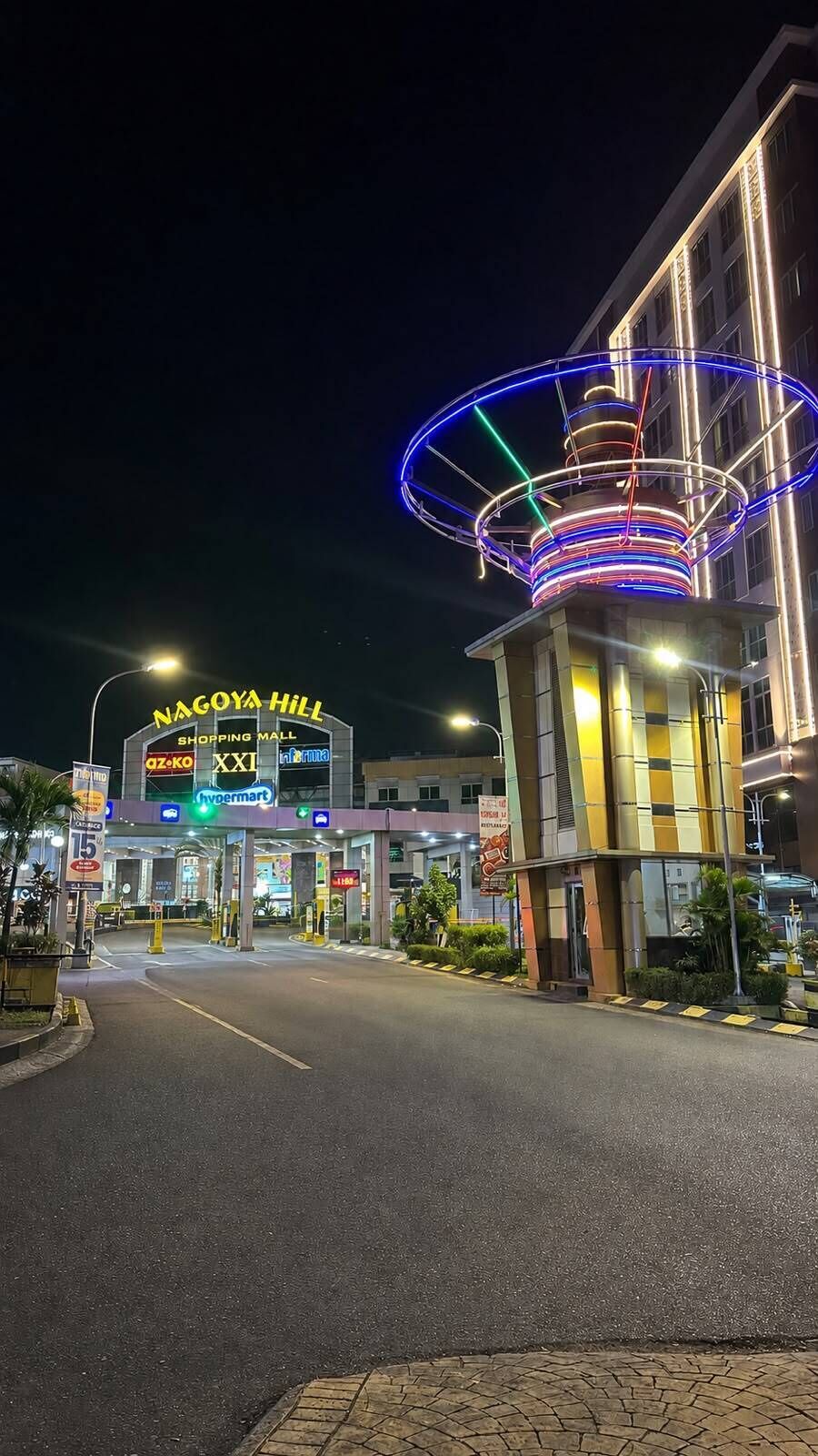 Eingang eines Einkaufszentrums mit einem gut sichtbaren Schild für 'NAGOYA HILL' und 'SHOPPING MALL', sowie erkennbaren Geschäften wie 'az-ko' und 'hypermart'.